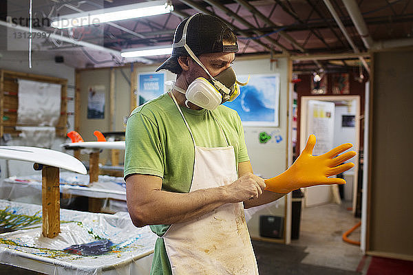 Männlicher Arbeiter zieht Handschuh an  während er in der Werkstatt steht