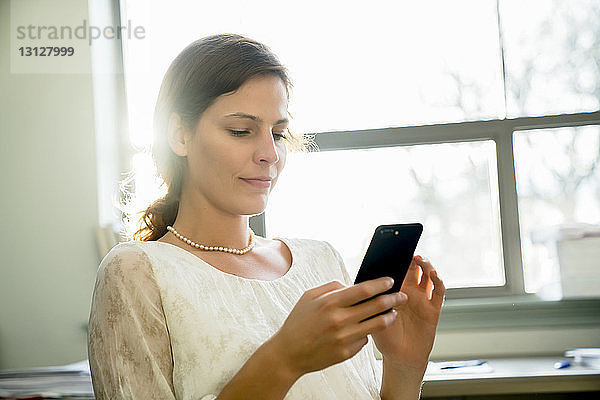 Geschäftsfrau benutzt Smartphone  während sie im Büro sitzt