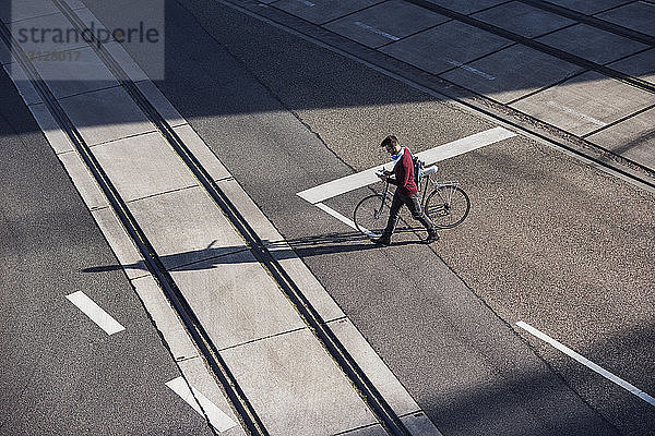 Hochwinkelansicht eines Mannes zu Fuß mit Fahrrad auf der Straße