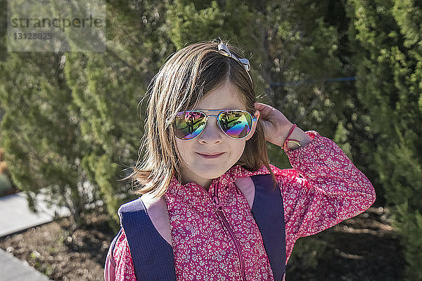 Nahaufnahme eines Mädchens mit Rucksack und Sonnenbrille  das an sonnigen Tagen vor Pflanzen steht