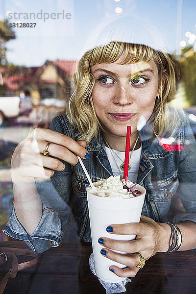 Nachdenkliche Frau schaut weg  während sie im Café ein Milchshake-Glas hält