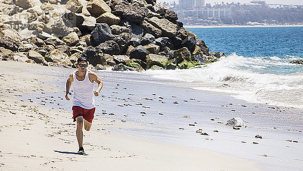 Mann mit Sonnenbrille joggt am Strand an einem sonnigen Tag