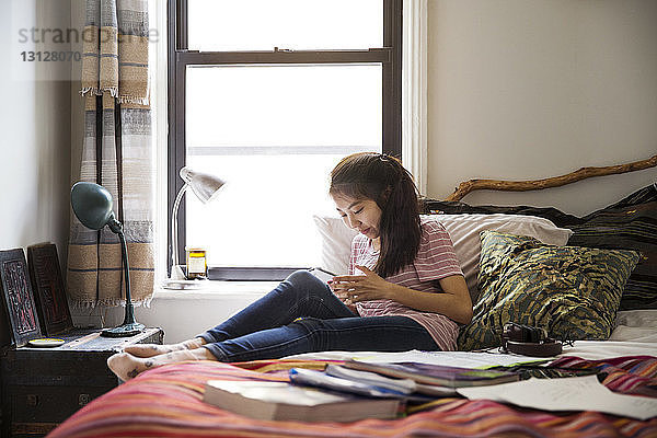 Teenagerin benutzt Smartphone  während sie sich im Bett entspannt