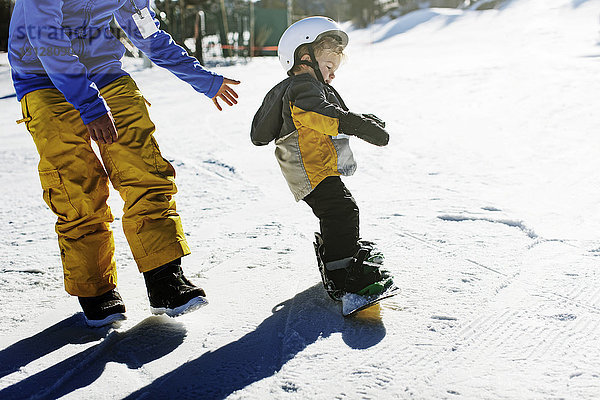 Hochwinkelansicht des Vaters  der der Tochter beim Snowboarden hilft