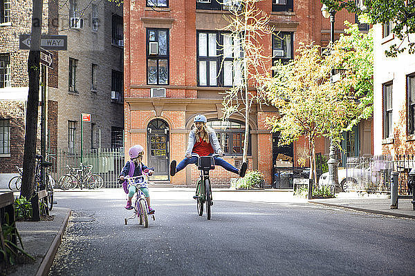 Fröhliche Frau fährt Fahrrad mit Tochter auf der Straße