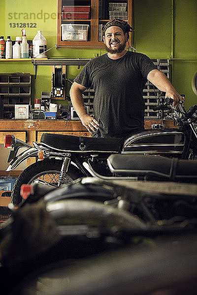 Porträt eines lächelnden Besitzers  der in der Werkstatt an einem Motorrad steht