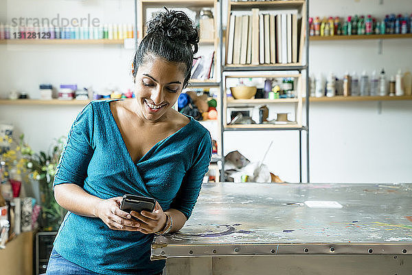 Glückliche Geschäftsfrau benutzt Smartphone  während sie sich im Büro auf den Tisch lehnt