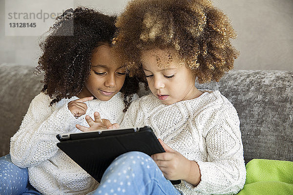 Schwestern benutzen digitales Tablet  während sie zu Hause auf dem Sofa sitzen