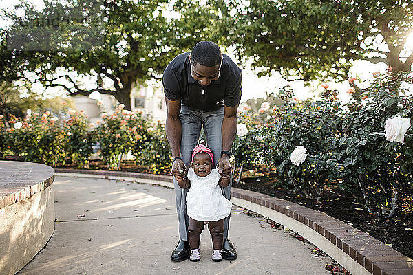 Vater hilft Tochter beim Stehen auf Fußweg im Park