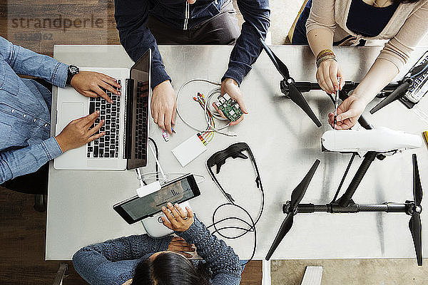 Draufsicht auf Schüler  die an elektrischen Geräten am Tisch im Klassenzimmer arbeiten