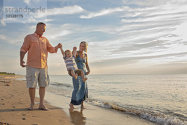 Verspielte Eltern halten die Hände ihres Sohnes  während sie ihn am Strand schaukeln