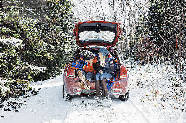 Freundinnen sitzen im Winter im Kofferraum eines Autos im Algonquin-Provinzpark