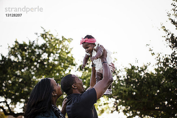 Niedriger Blickwinkel auf glückliche Eltern  die mit ihrer Tochter spielen  während sie im Park gegen den Himmel stehen