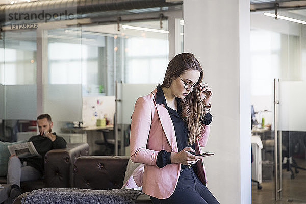 Frau benutzt Mobiltelefon  während ein Kollege im Büro Zeitung liest