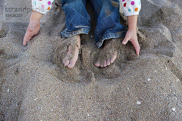 Niedriger Abschnitt eines Mädchens  das am Strand im Sand spielt