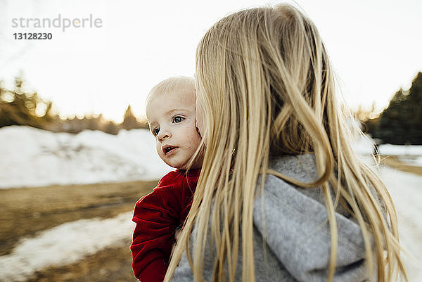 Mädchen küsst Bruder  während sie im Winter auf dem Feld steht