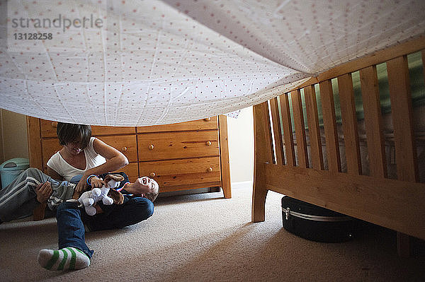 Mutter und Sohn spielen unter Textilien im Schlafzimmer