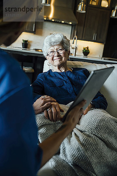 Ausgeschnittenes Bild einer häuslichen Pflegekraft  die einer älteren Frau im Wohnzimmer einen Tablet-Computer zeigt
