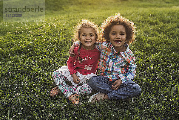 Porträt von lächelnden Geschwistern  die auf einem Grasfeld im Park sitzen