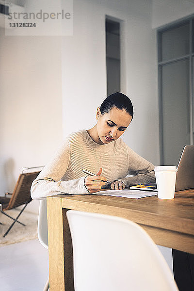 Geschäftsfrau schreibt  während sie im Büro am Schreibtisch sitzt