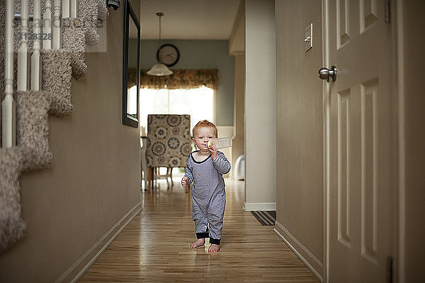 Porträt eines süßen Jungen  der Milch aus der Flasche trinkt  während er zu Hause auf dem Boden steht