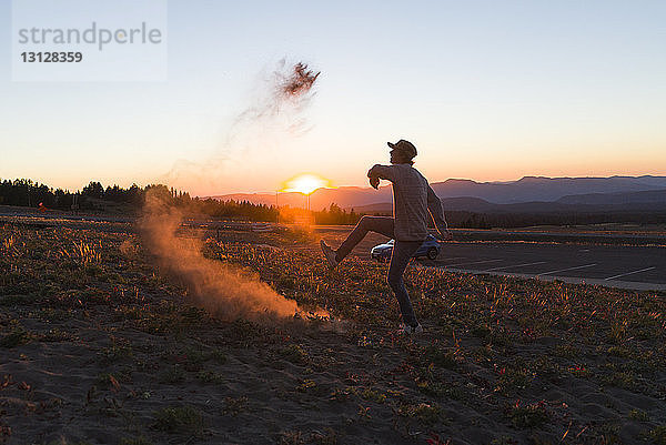 Seitenansicht eines glücklichen Mannes  der bei Sonnenuntergang auf dem Feld gegen den Himmel tanzt