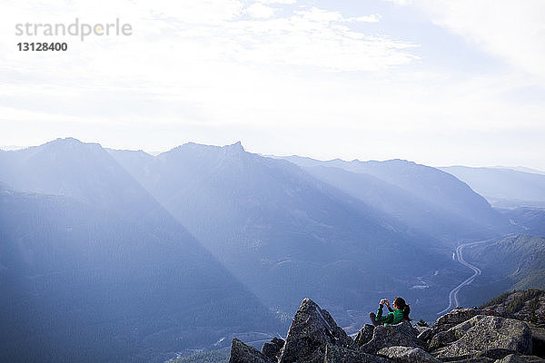 Hochwinkelaufnahme einer Frau  die auf Felsen sitzend vor einer Bergkette fotografiert