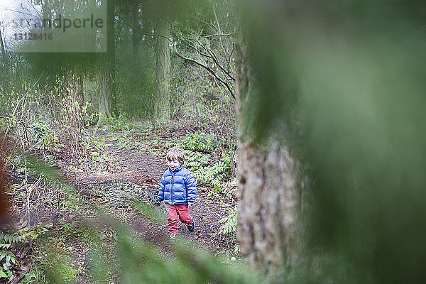 Hochwinkelaufnahme eines glücklichen Jungen  der im Wald spazieren geht