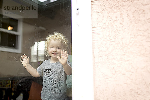 Porträt eines süßen Jungen  der zu Hause steht und durch ein Fenster gesehen wird