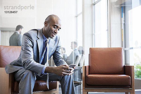 Glücklicher Geschäftsmann benutzt ein Smartphone  während er im Büro sitzt