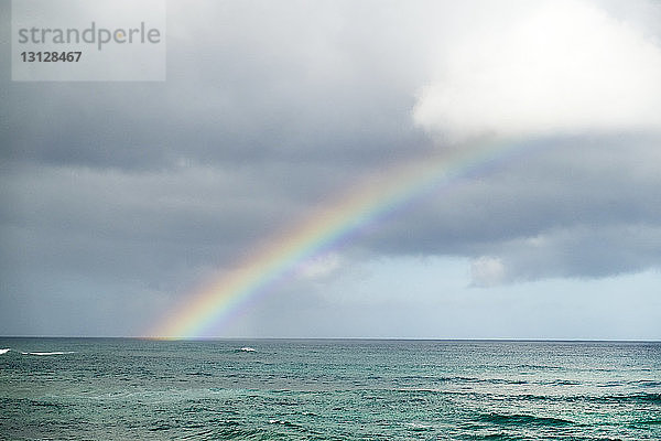 Idyllische Ansicht des Regenbogens über dem Meer vor bewölktem Himmel