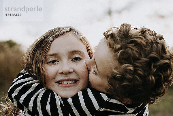 Nahaufnahme einer lächelnden Schwester mit einem liebenden Bruder  der sie im Park küsst
