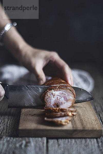 Beschnittenes Bild einer Frau  die zu Hause auf einem Schneidebrett char sui Schweinefleisch schneidet