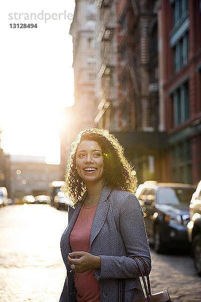 Glückliche Geschäftsfrau schaut weg  während sie auf der Straße der Stadt steht