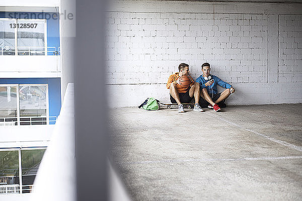 Männliche Freunde mit Basketball und Skateboard auf dem Parkplatz