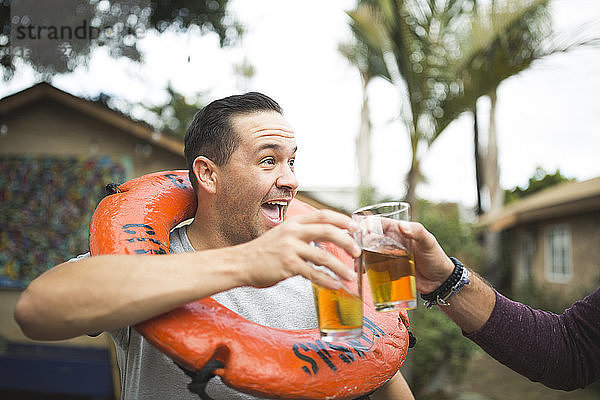 Beschnittenes Bild einer Hand  die mit einem glücklichen Freund auf ein Bierglas anstößt  während sie im Hinterhof steht