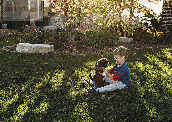 Glücklicher Junge spielt mit Hund auf Grasfeld im Hinterhof