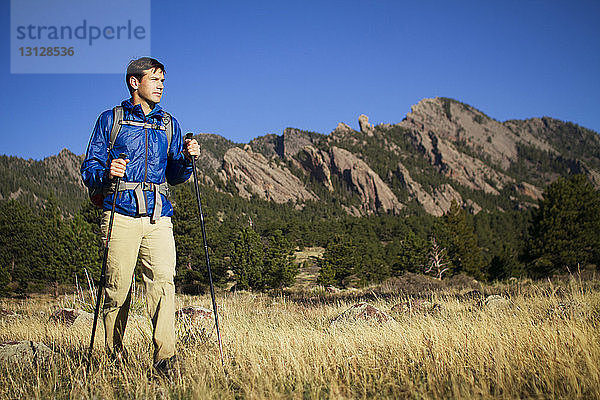 Mann steht auf Feld und hält Wanderstöcke gegen Berge