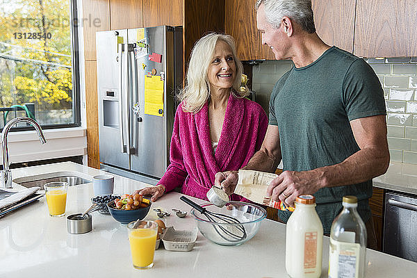 Lächelnder Mann schaut Frau an  während er in der Küche Essen zubereitet