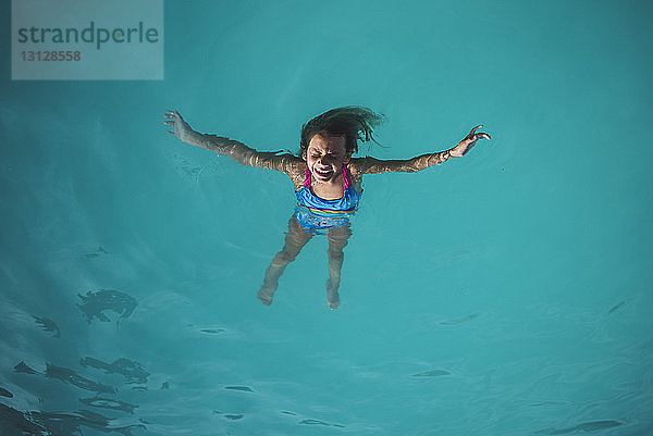 Hochwinkelaufnahme eines sorglosen Mädchens  das im Schwimmbad auf dem Wasser schwimmt