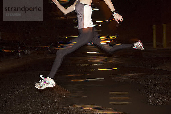 Unterer Teil einer Joggerin  die nachts in der Stadt über eine Pfütze springt