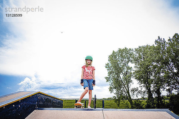 Porträt eines Skateboard fahrenden Mädchens vor bewölktem Himmel im Park