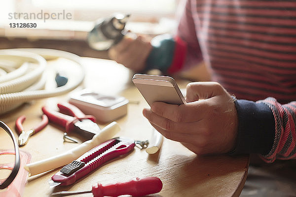 Mittelsektion eines Mannes mit Smartphone im Workshop