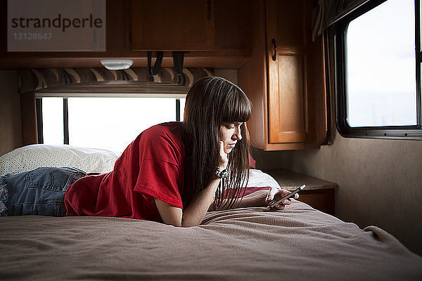 Junge Frau benutzt Smartphone  während sie sich im Wohnmobil im Bett entspannt