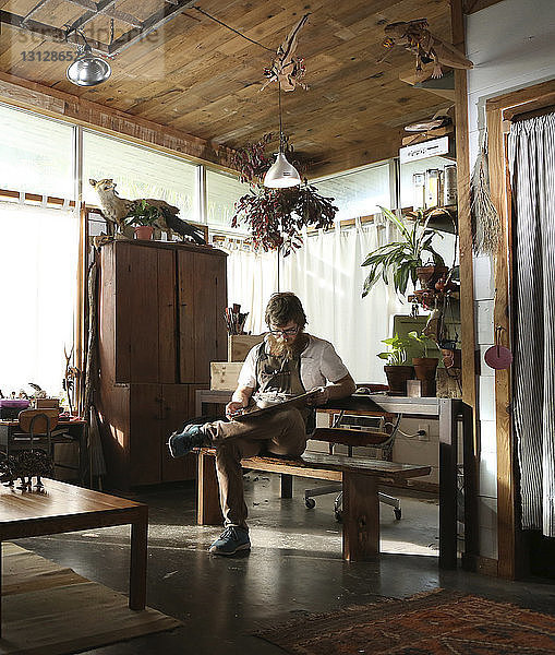 Tischler liest Dokument in voller Länge  während er in der Werkstatt auf einer Bank sitzt