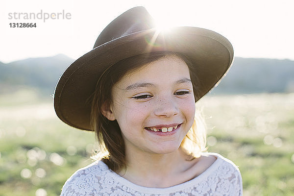 Nahaufnahme eines glücklichen Mädchens  das einen Hut trägt  während es am sonnigen Tag gegen den Himmel steht