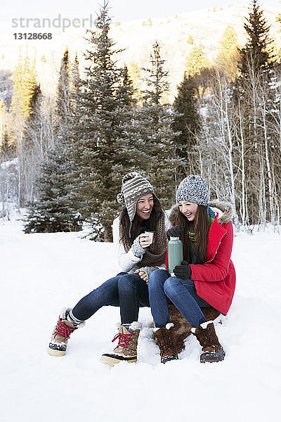 Fröhliche Familie hält Kaffee  während sie auf einem Felsen im verschneiten Feld sitzt