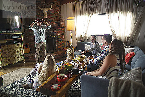 Glückliche Freunde schauen den Menschen an  während sie beim geselligen Beisammensein zu Hause ein Heads-up-Spiel spielen