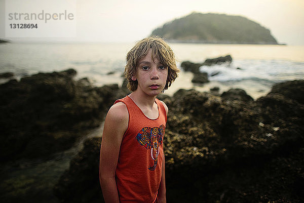 Porträt eines Jungen  der bei Sonnenuntergang am Meer steht