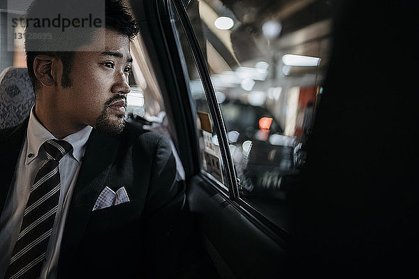 Nachdenklicher Geschäftsmann schaut im Taxi durchs Fenster
